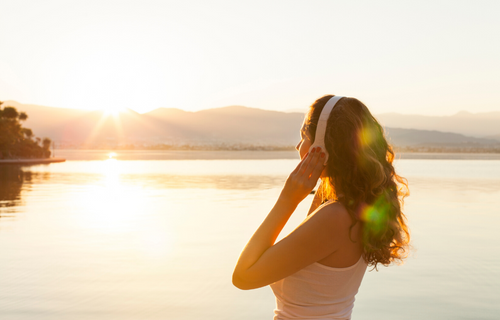 Mujer en un atardecer mirando el horizonte de un lago mientras escucha música 