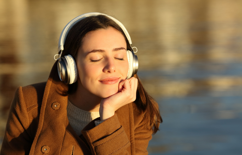 Mujer escuchando música con audífonos con un lago detrás